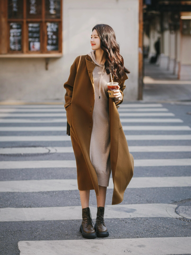 栗色长款羊绒大衣搭配米色卫衣连衣裙和深棕色马丁厚底靴.