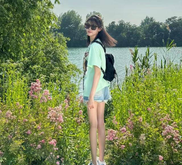 墨镜,身穿绿色印花t恤搭配牛仔热裤,脚踩运动鞋,背上挎着一个黑色小包