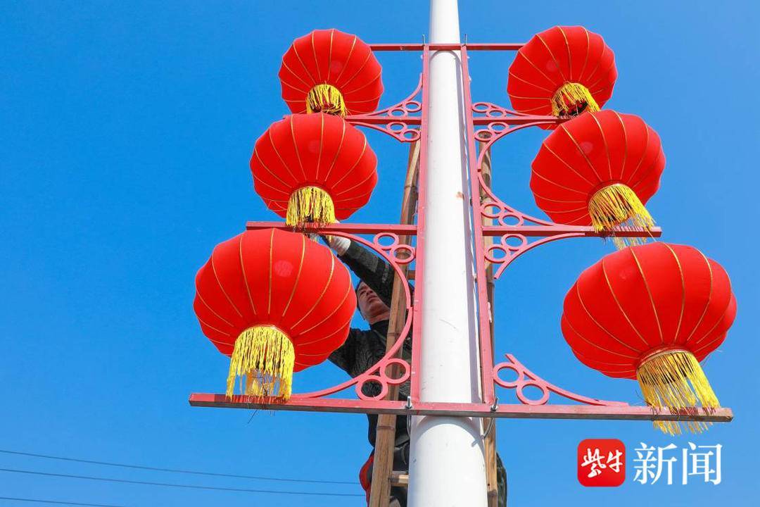工人们正忙在集镇道路旁的路灯杆上悬挂红彤彤的大灯笼
