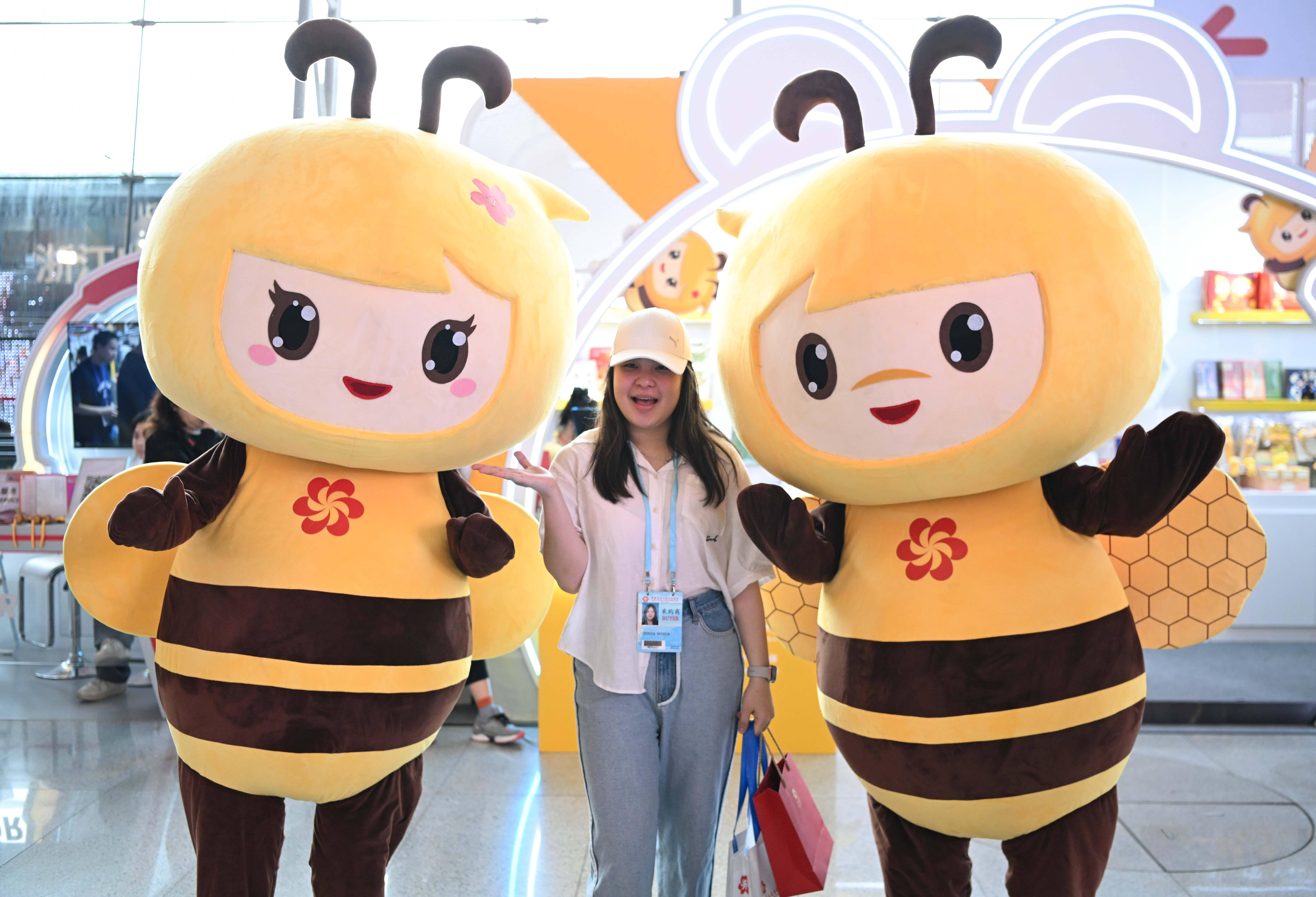 4月23日,境外采购商在广交会展馆与吉祥物合影留念.